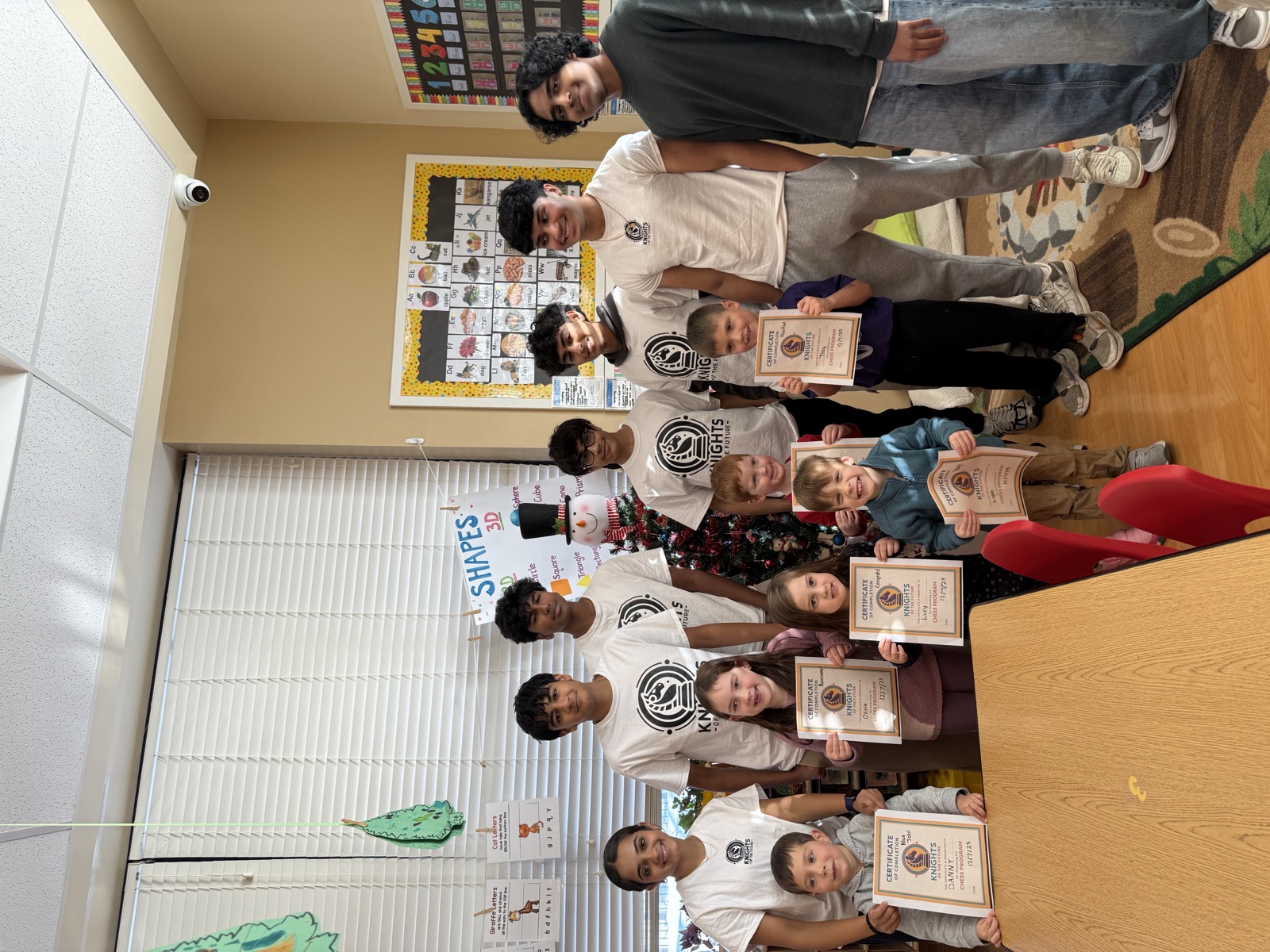 Chess mentors standing with young students, each child holding a Knights of the Future certificate of completion.