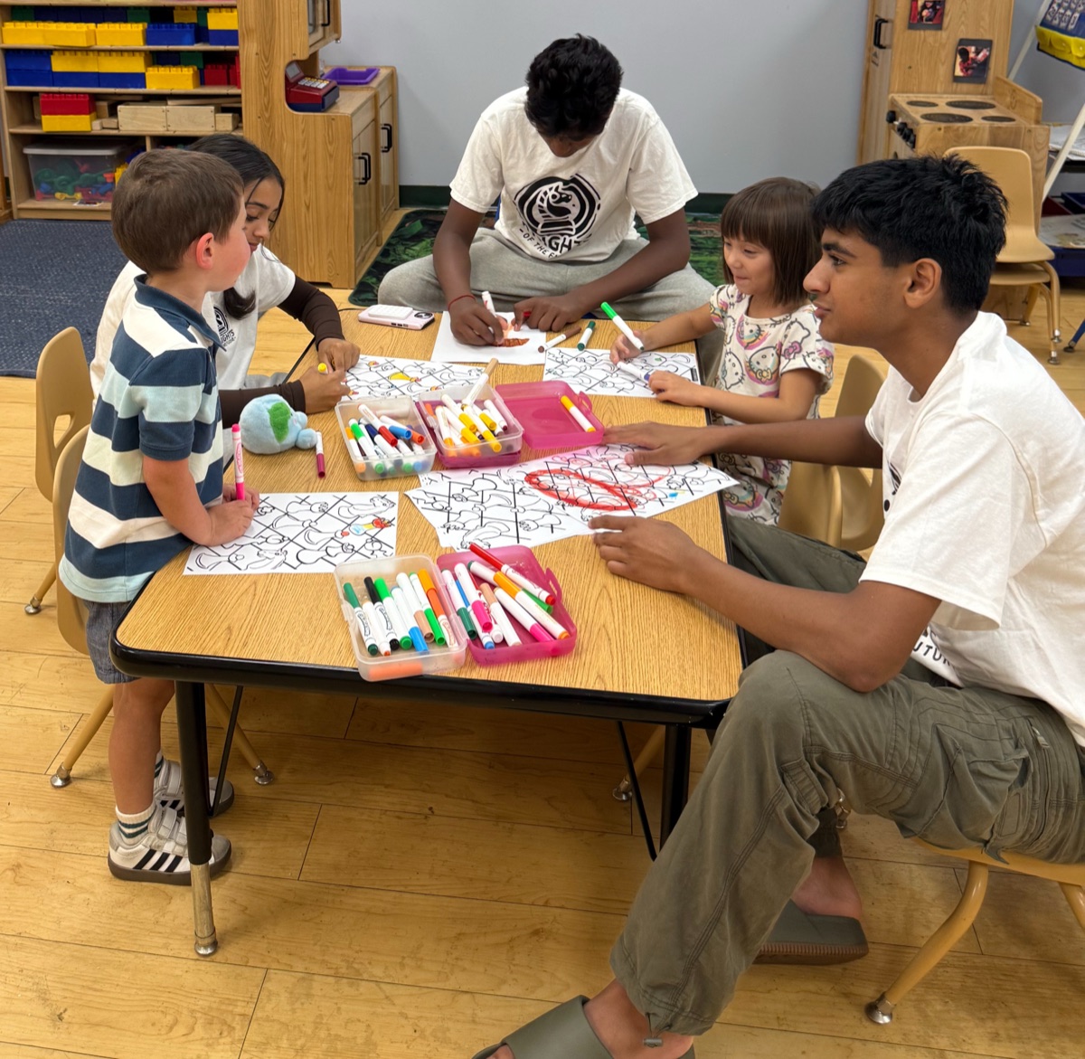 A mentor working through chess worksheets at a table with two young students.